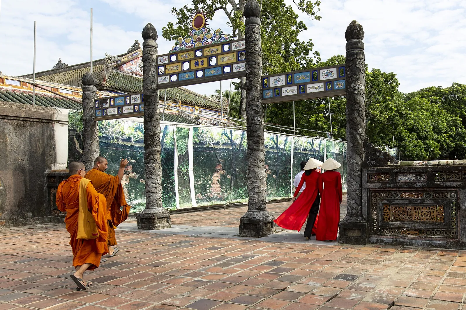 Ao dai rosso nella cittadella imperiale di Hue Due donne vietnamite in ao dai rosso con cappello di paglia attraversano un cancello della cittadella imperiale di Hue insieme a due monaci buddisti