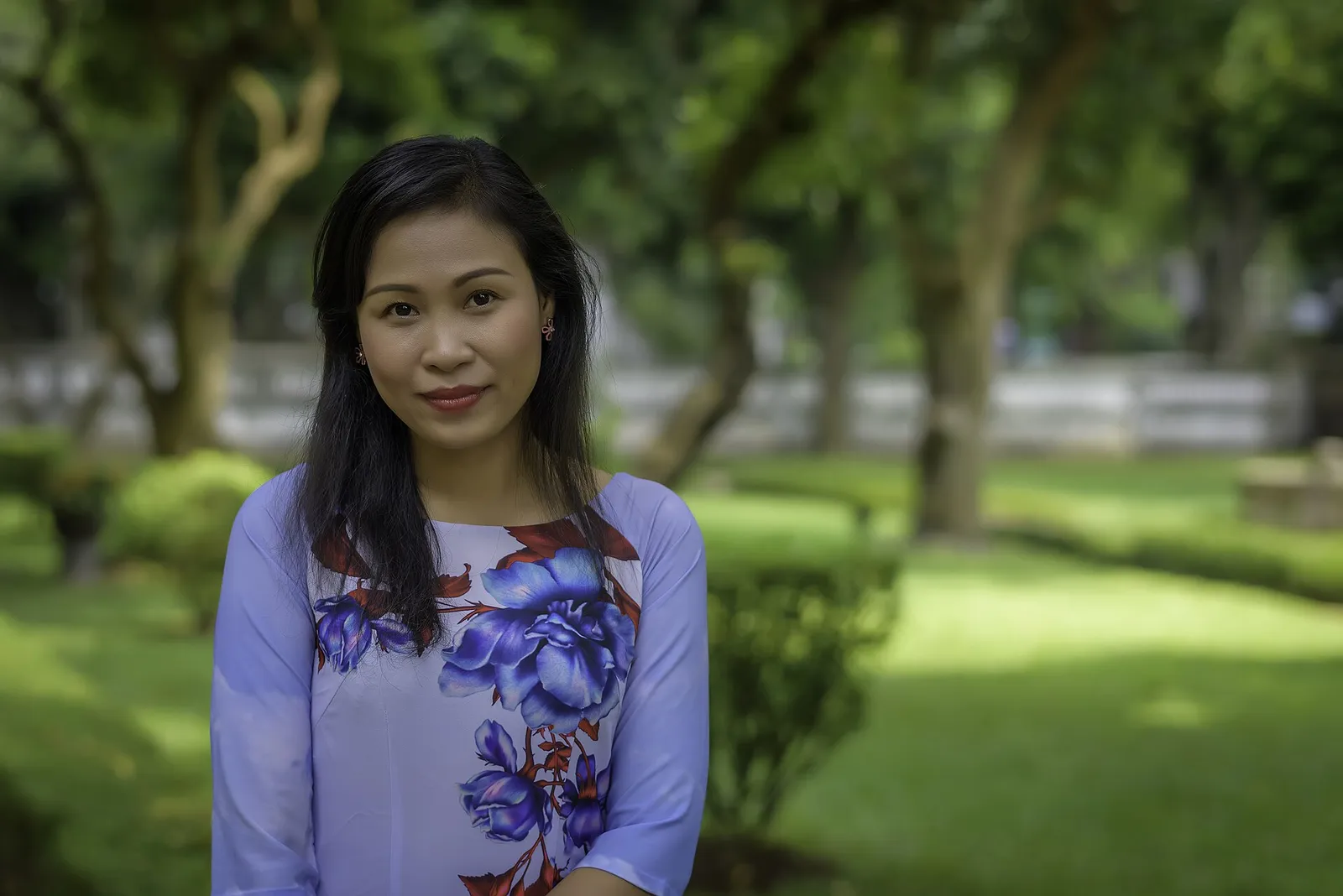 La versione moderna dell'ao dai Giovane donna vietnamita con un ao dai moderno a fiori blu in un giardino di Ho Chi Minh City, versione contemporanea dell'abito tradizionale vietnamita