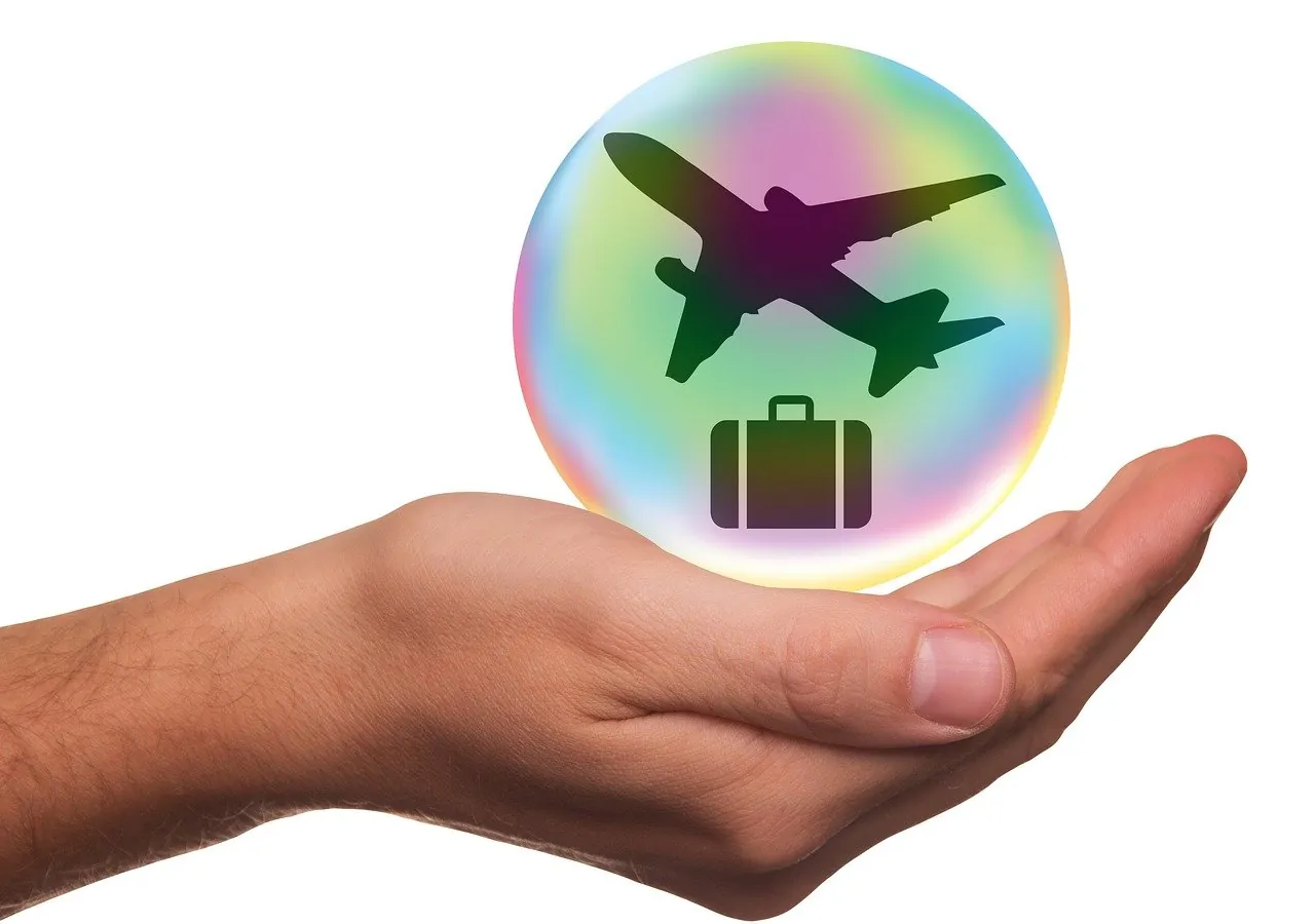 Mano che accoglie un mappamondo con aeroplano e valigia stilizzati: assicurazione di viaggio