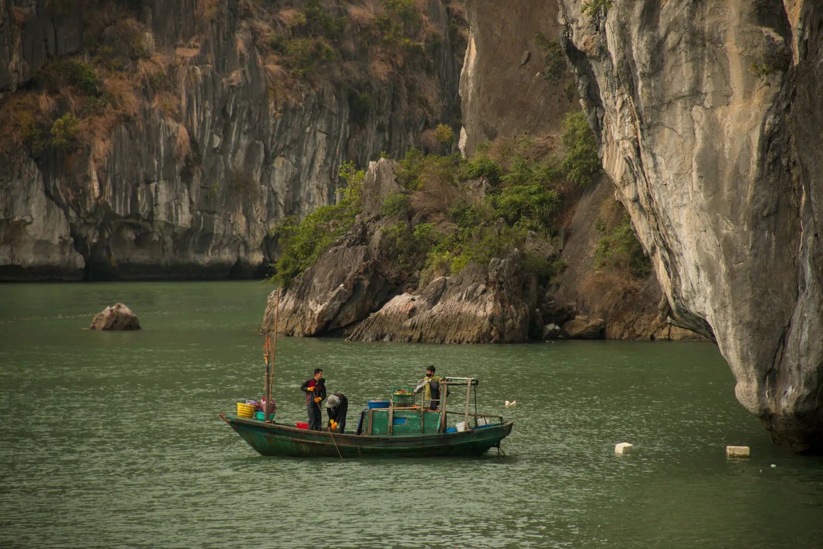 Barca di pescatori tra i faraglioni calcarei di Bai Tu Long Bay, l'alternativa autentica alla Baia di Halong