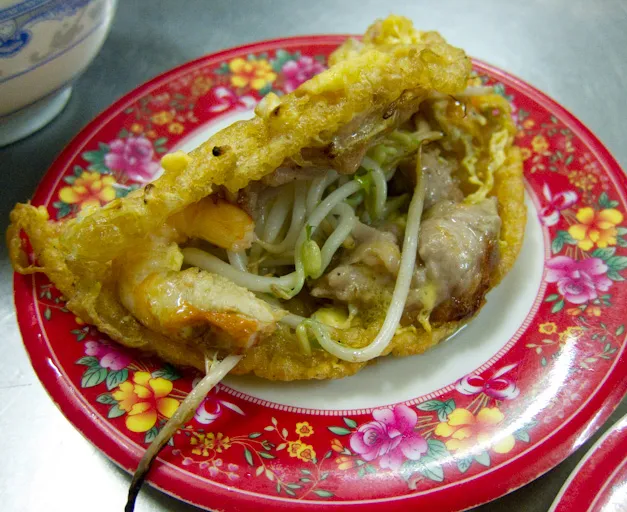 Un banh khoai, pancake croccante vietnamito tipico della cucina di Hue, ripieno di gamberi, maiale e germogli di soia su un piatto floreale rosso