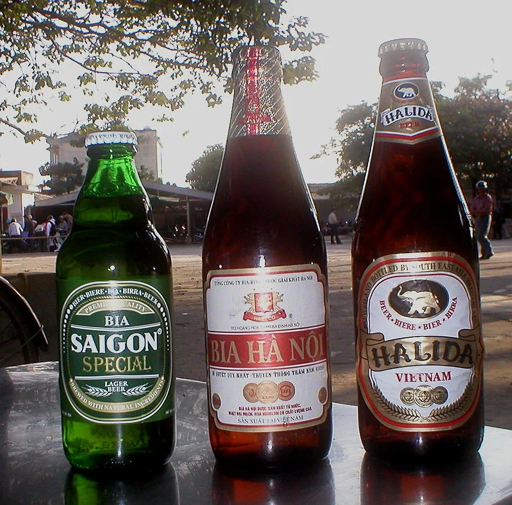 Tre birre vietnamite in bottiglia, Saigon Special, Bia Ha Noi e Halida, su un tavolo all'aperto