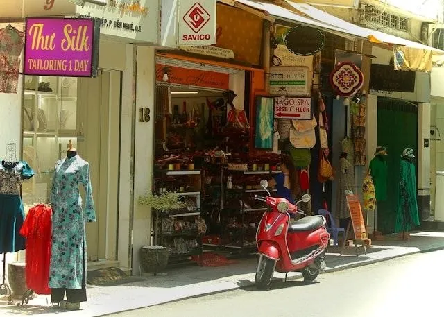 Vetrina di una sartoria con ao dai e scooter rosso Vetrina di una sartoria con un ao dai esposto su un manichino e uno scooter rosso parcheggiato davanti