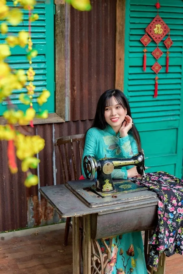 Sarta con ao dai e macchina da cucire Singer a Hoi An Giovane sarta vietnamita in ao dai turchese seduta dietro una macchina da cucire Singer antica a Hoi An