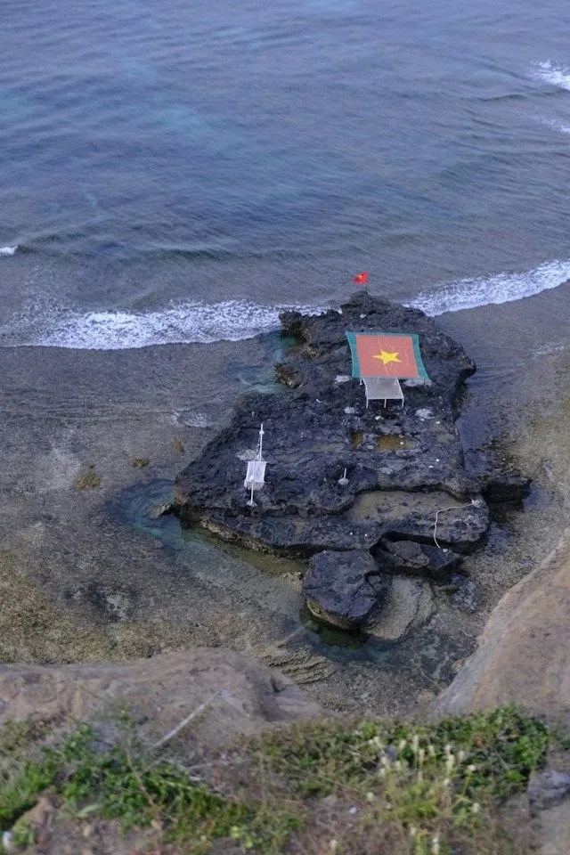 Scogliera di lava nera di Ly Son con la bandiera vietnamita sul mare cristallino