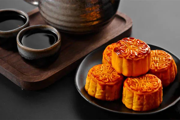 un piatto di dolci, mooncakes accanto a un vassoio con tazze di tè