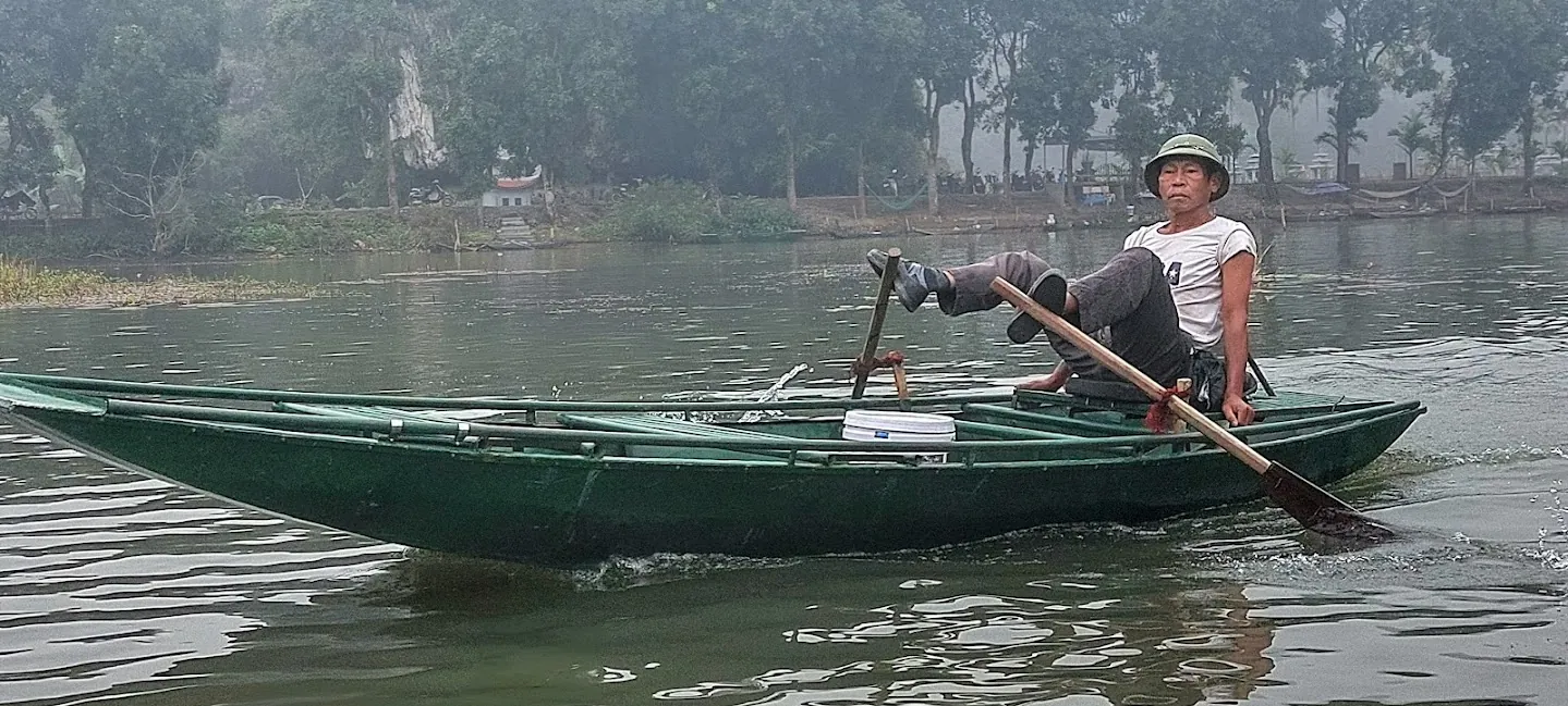Barcaiolo che voga con i piedi su una barca di legno a Tam Coc
