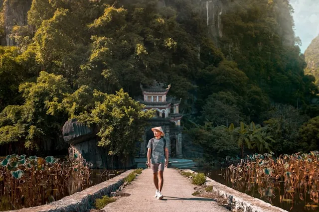 Turista passeggia su un ponte di legno davanti a una collina rocciosa a Ninh Binh