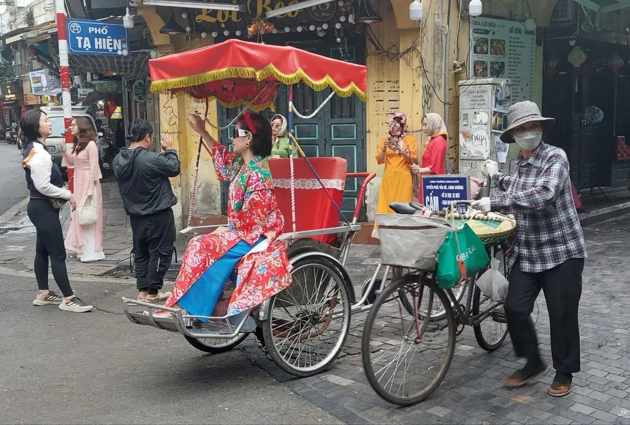Cyclo con cupola rossa e donna in abito tradizionale in via Ta Hien, nel quartiere vecchio di Hanoi, con venditore ambulante in bicicletta