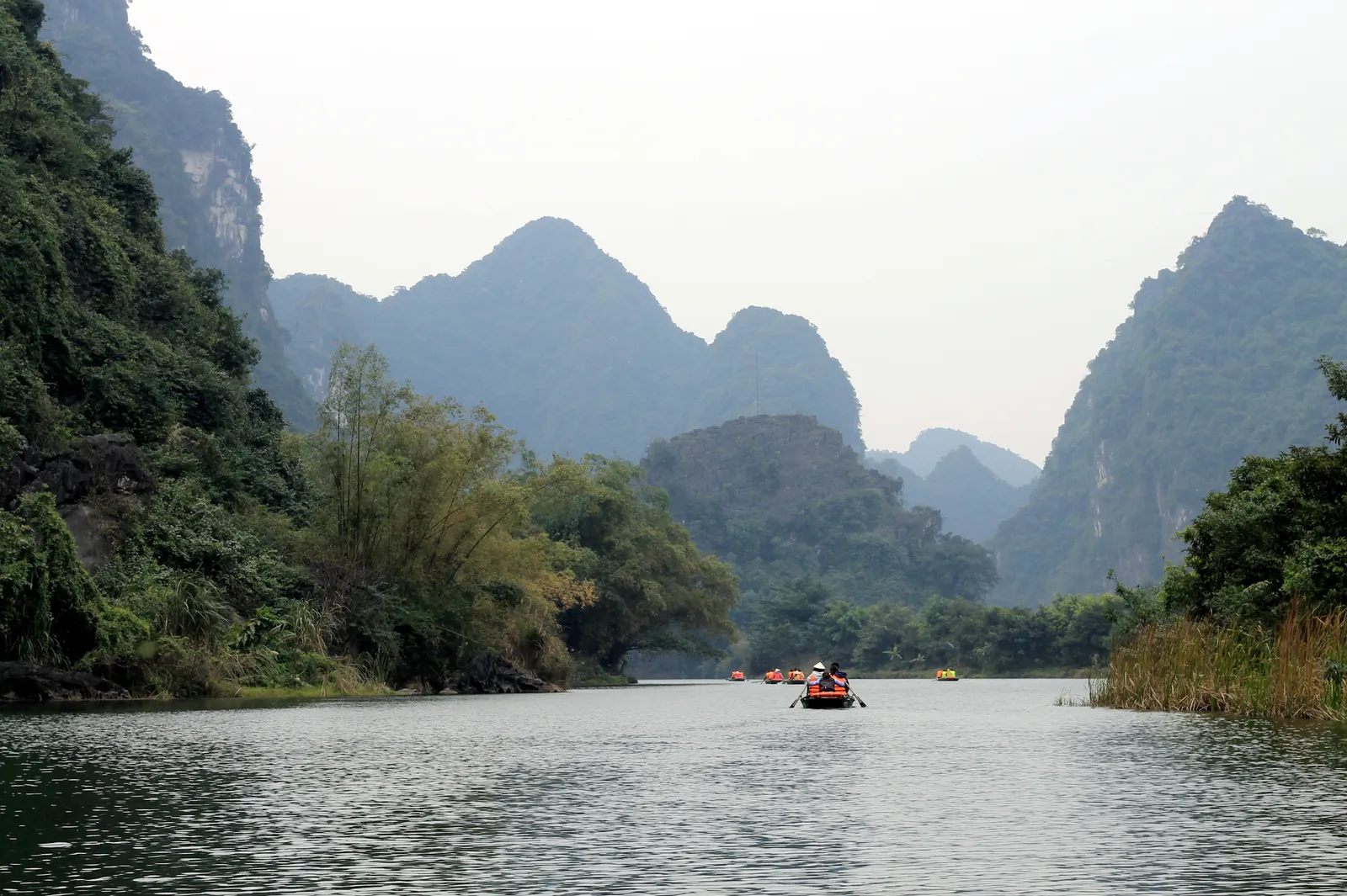 Barca sul fiume di Tam Coc Giro in barca a Tam Coc, Ninh Binh: una barca a remi con i turisti naviga verso le grotte del fiume tra le montagne calcaree