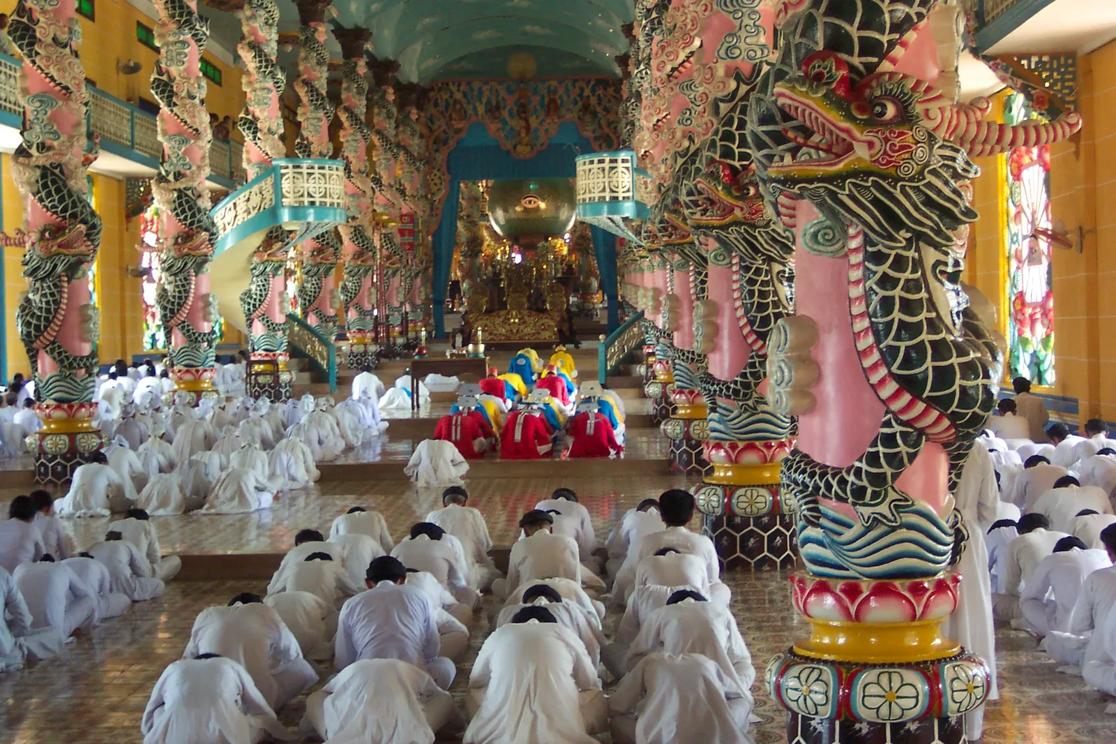 Interno del Santuario Cao Dai con colonne decorate e fedeli in preghiera
