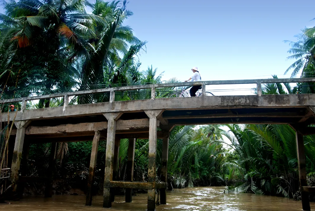 Ragazza in bicicletta accanto a un vecchio ponte nel Delta del Mekong, Vietnam