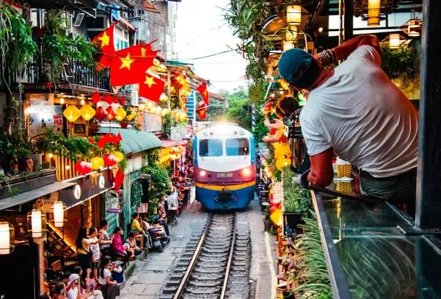 Train Street di Hanoi Treno in transito nella celebre Train Street di Hanoi, la via stretta con i binari al centro tra caffè e bandiere vietnamite