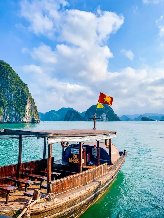 Barca turistica nella baia di Ha Long Barca turistica in legno con la bandiera vietnamita tra le isolette carsiche della baia di Ha Long